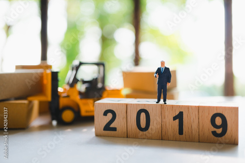 Miniature people, businessman standing on wooden block year 2019 with logistic vehecle background using as business and logistics concept photo