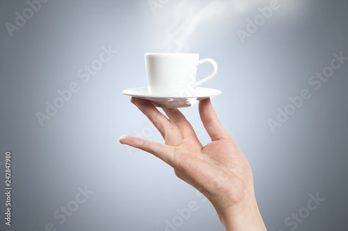Aristocratic hand holding a small cup of coffee or tea on grey background
