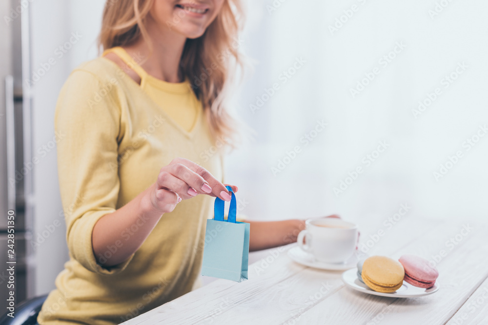 cropped view of woman holding small shopping bag near cup and macaroons cropped view of woman holding small shopping bag near cup and macaroons
