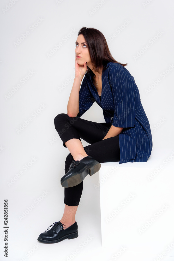 Concept portrait of a girl standing on a white background in a business suit in different poses with different emotions. It in the middle of the frame, next to the white cubes, next is another cube.
