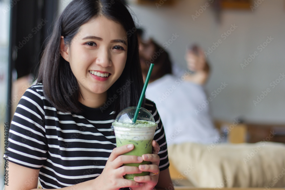 Smiling woman drinking matcha green tea latte in the morning at coffee shop. Portrait pretty Asian girl holding green tea glass in cafe. Smiling woman drinking matcha green tea latte in the morning at coffee shop. Portrait pretty Asian girl holding green tea glass in cafe.