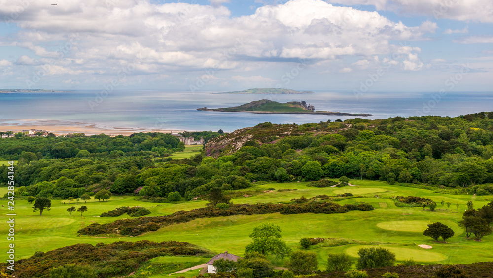 Beautiful landscape of green hills covered in grass and trees at the sea shore. View from the Deer Park Golf  in Howth, Dublin with the Ireland's Eye, a small island, in the distance.