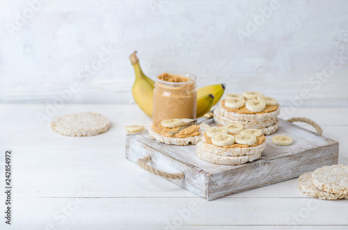 Healthy breakfast with rice cakes with peanut butter and slices of banana on white wooden table. Space for text.