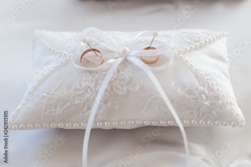 A pair of wedding rings on a white pillow. In the center of the pillow is a ribbon bow. Close-up