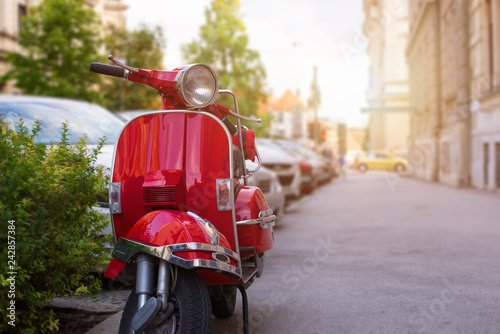 Retro red scooter on street of the European city. Summer sun light in background. Copy space beside.