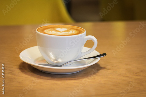 White porcelain cup of coffee with a saucer and a spoon on a wooden table.