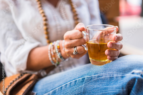 Close up of woman hands taking chamomil camomilla glass to warm up and relax - casual jeans and whit eshirt - outdoor leisure activity - drinking healthy lifestyle positive vibes