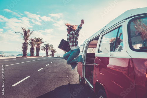 Happiness for travel and enjoying wanderlust concept for beautiful curly crazy woman jumping out the old van with vintage luggage - joyful and success lifestyle for alternative hipster people photo