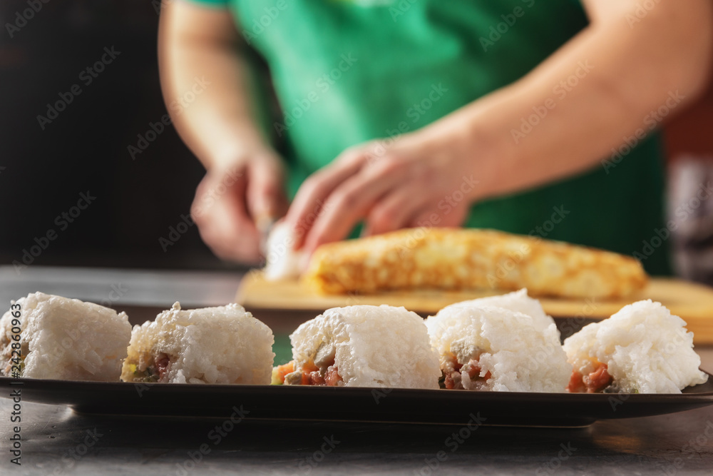 a knife in his hand cuts a roll of rice. closeup on a wooden board