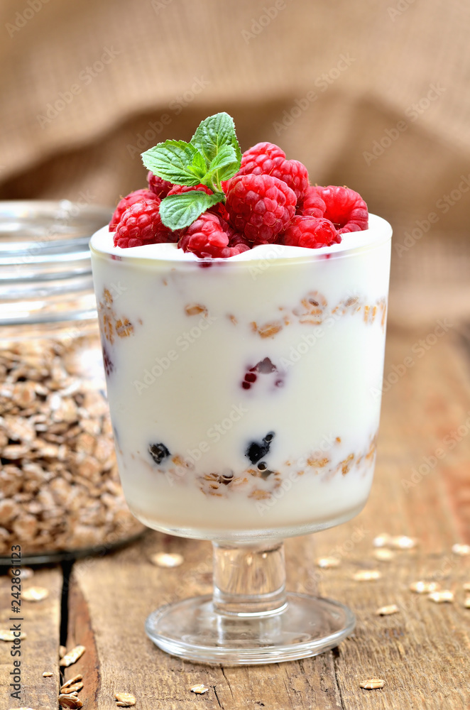Greek yoghurt with oatmeal and fresh raspberries in a glass and mint leaves - vertical photo Greek yoghurt with oatmeal and fresh raspberries in a glass and mint leaves - vertical photo