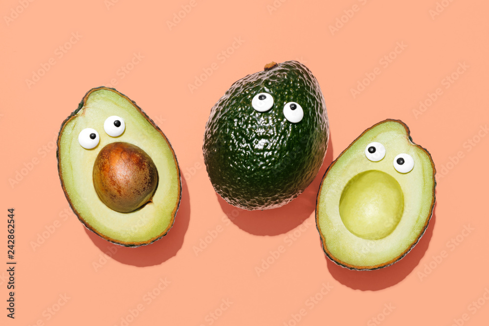 Funny faces avocados on a pastel peach background, creative healthy food concept, top view with clipping path