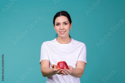Young attractive woman in t-shirt holding a red apple in her hands and giving it to you. Healthy vegetarian food concept. Spring Avitaminosis prevention.