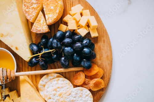Flat lay with various types of cheese, grapes, nuts, honey and cracker in wooden board on marble