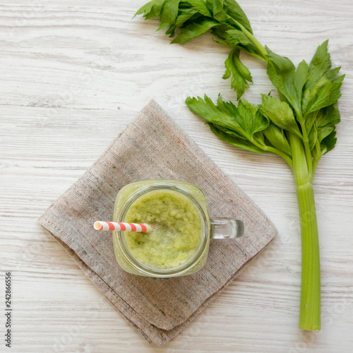 Green celery smoothie in glass jar over white wooden surface, top view. Flat lay, from above, overhead.