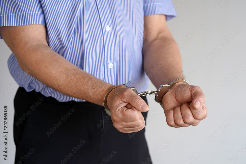 Close-up. Arrested elderly man handcuffed hands isolated on gray background. Prisoner or arrested terrorist, close-up of hands in handcuffs.