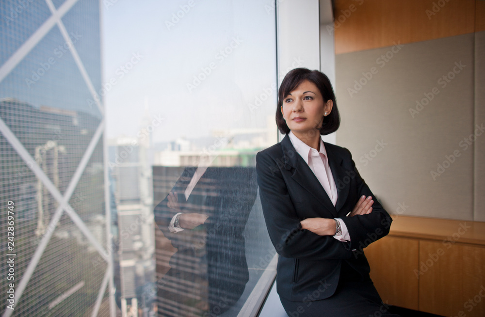 Contemplative businesswoman looking out an office window this her arm folded. Contemplative businesswoman looking out an office window this her arm folded.