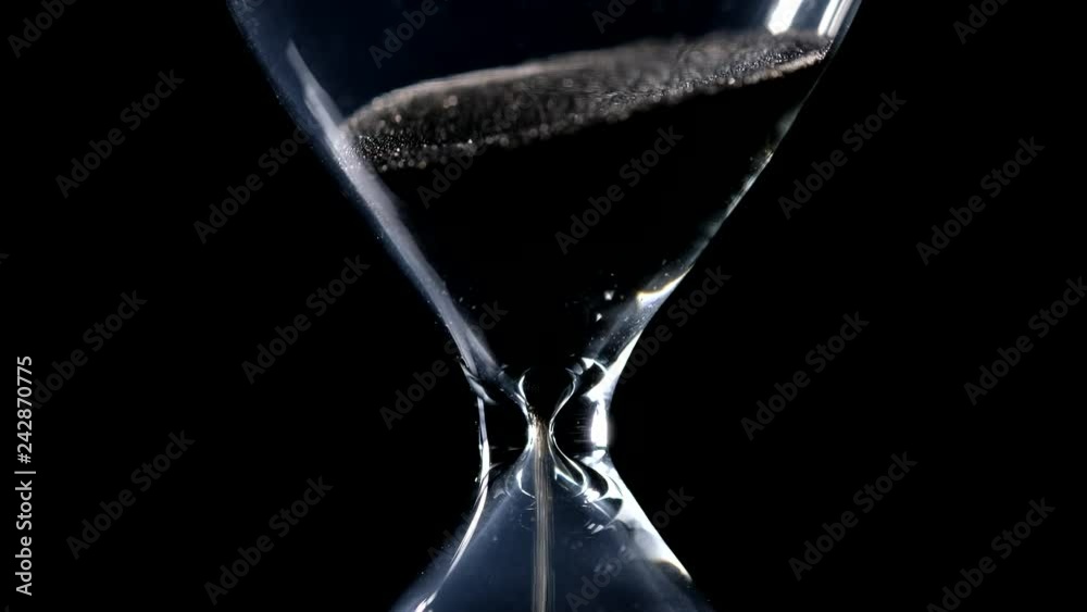 The sand flow in the hourglass with black background and lateral light backlight in centered composition