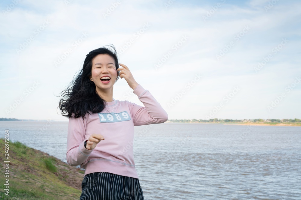 Asian CASUAL woman laughing on a grassland posing at a riverside blue sky view background. Portrait of young Happy woman against grassland with river background. - relaxing concept. Asian CASUAL woman laughing on a grassland posing at a riverside blue sky view background. Portrait of young Happy woman against grassland with river background. - relaxing concept.