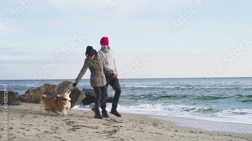 Young couple walking on the beach with cute corgi dog