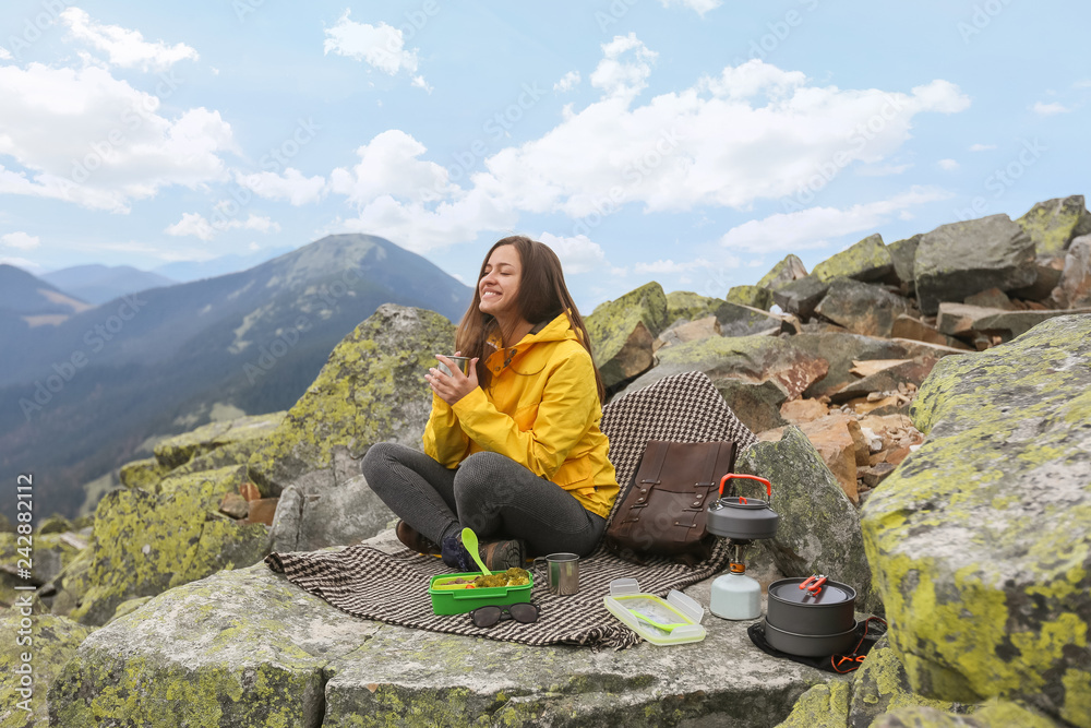 Young woman in yellow jacket have a picnic on top of the mountain. 