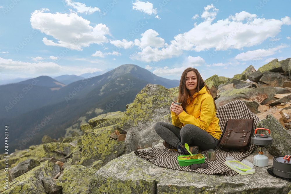 Young woman in yellow jacket have a picnic on top of the mountain. 