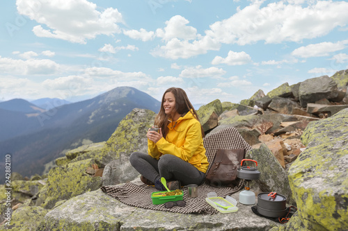 Young woman in yellow jacket have a picnic on top of the mountain. 