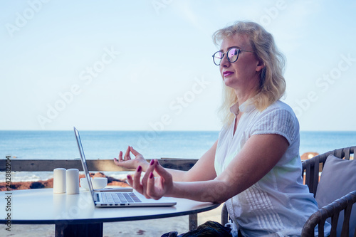 attractive woman of 40years with a mobile phone and laptop at the beach cafe on the background of the sea.remote work freelancer business blonde woman