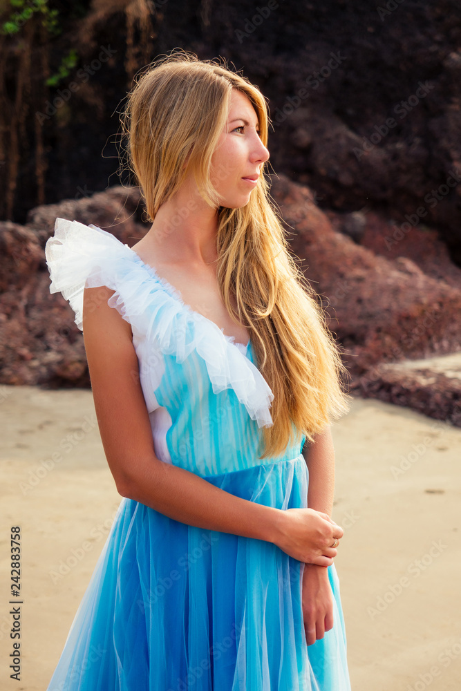 Young beautiful caucasian blonde woman in long tull butterfly white blue dress on coast of sea.female running towards the ocean freedom Young beautiful caucasian blonde woman in long tull butterfly white blue dress on coast of sea.female running towards the ocean freedom