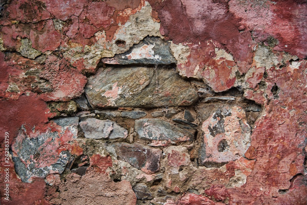 Antique colonial stone wall, with a colorful rough and peeling texture in red unpainted tones. Antique colonial stone wall, with a colorful rough and peeling texture in red unpainted tones.