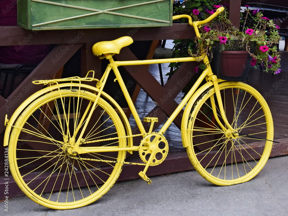 Yellow bicycle with a basket of flowers outdoors. Retro decor