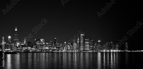 Long-exposure photo of downtown Chicago at night. The light of the stars can be see in the clear sky above  and the reflection of the city lights is in the lake in the foreground.
