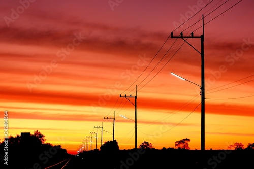 Silhouette row of street lights on electric poles with cable lines on the road and railway in landscape view with blur altostratus clouds in colorful twilight sky background