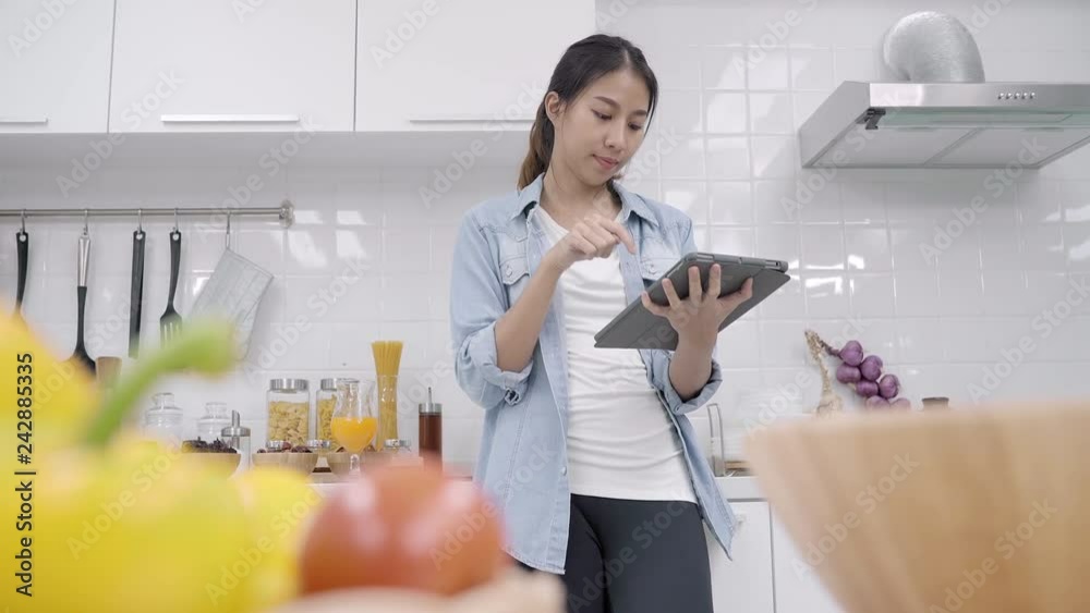 Happy Asian woman using tablet for looking recipe while making food in the kitchen, female use organic vegetable for healthy food at home. Lifestyle women making food concept. Happy Asian woman using tablet for looking recipe while making food in the kitchen, female use organic vegetable for healthy food at home. Lifestyle women making food concept.