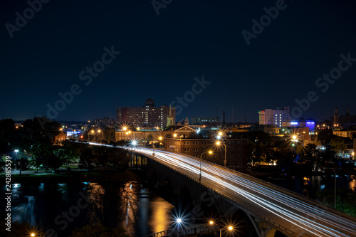 Nighttime overhead city downtown urban area with bridge and light trails of passing vehicles in foreground.