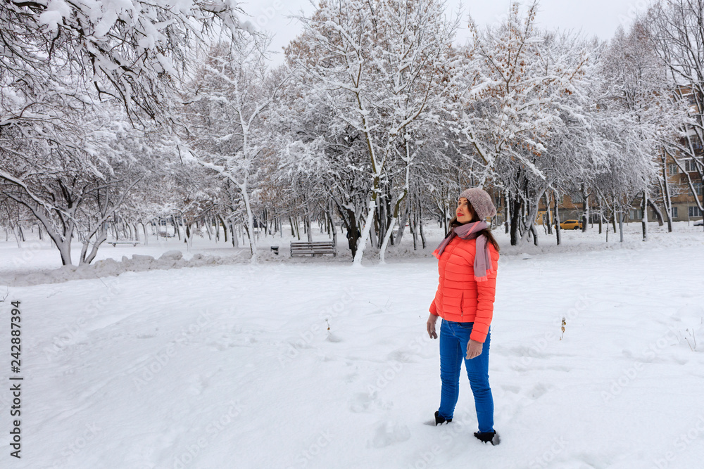 Shot of a happy and stylish beautiful woman in a bright coral jacket and blue jeans, smiling, enjoying the winter day. Shot of a happy and stylish beautiful woman in a bright coral jacket and blue jeans, smiling, enjoying the winter day.