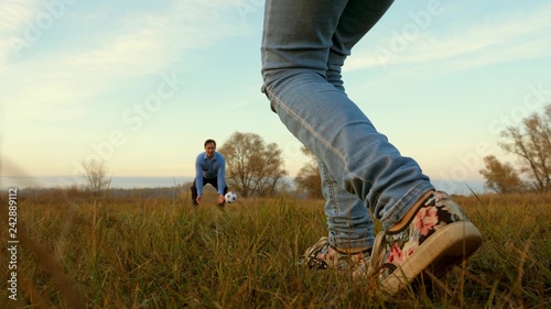 girl's leg hits soccer ball man catches ball. family plays football in park. dad and daughter play ball on field.