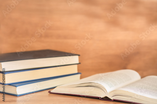 Open book with pile of closed books on wooden background.