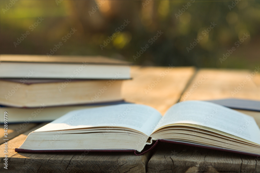 Pile of closed book with open book outdoors on wooden background Pile of closed book with open book outdoors on wooden background