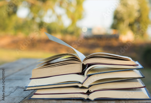 Pile of closed book with open book outdoors on wooden background