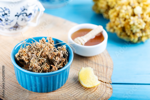 Dried linden flowers in bowl with honey and lemon on wooden background photo