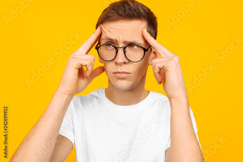 Portrait of a thoughtful dreamy guy with glasses and a white T-shirt  imagines something in mind  on a yellow background