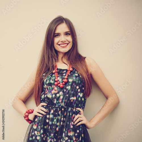 Portrait of smiling brunette woman wearing stylish dress and necklace, image with warm vintage toning and square aspect ratio