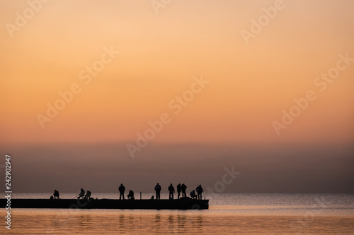 Silhouette of people fisherman on pier while beautiful sea sunset or dawn