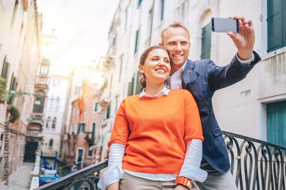 Fototapeta premium Szczęśliwa para zakochanych robi selfie na jednym z licznych mostów w Wenecji we Włoszech. Podróż do zdjęcia koncepcyjnego „miasta mostów”.
