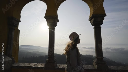 Woman walking on terrace of ancient palace in mountain. Silhouette girl in backlight enjoying beautiful view above green hills and town Sintra, Portugal photo
