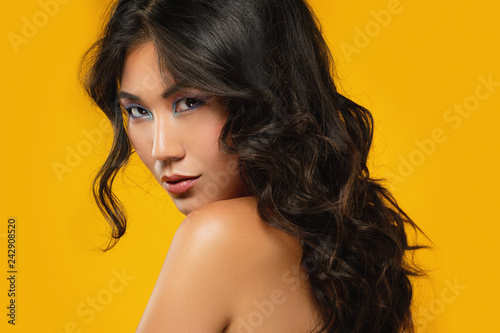 Asian woman with a beautiful curly hair and make-up on yellow background