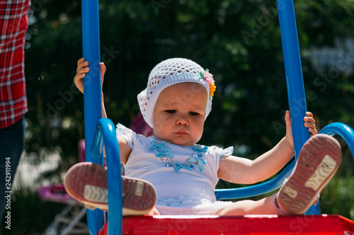 sad, little girl in a white dress and hat, riding on a swing, summer sun and heat. playground.childhood, serenity. negative emotions, anger