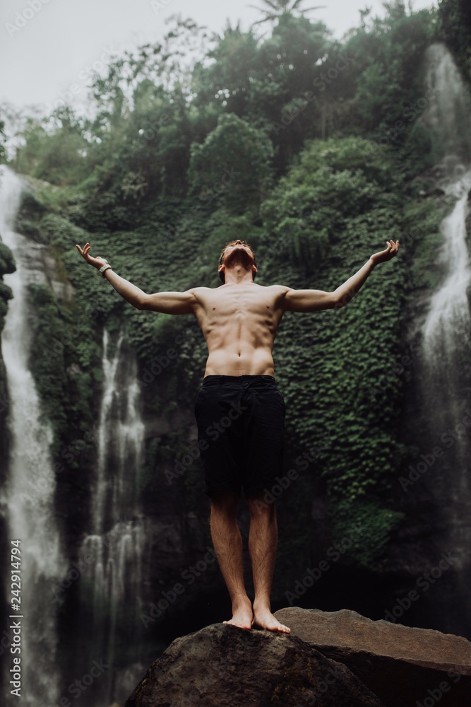 young man muscular and beautiful standing near the waterfall like Jesus.