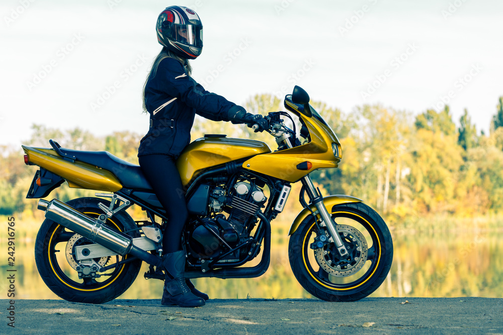 The girl in full equipment sits on a yellow motorcycle. The girl in full equipment sits on a yellow motorcycle.