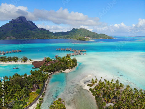 Aerial panoramic landscape view of the island of Bora Bora in French Polynesia with the Mont Otemanu mountain surrounded by a turquoise lagoon, motu atolls, reef barrier, and the South Pacific Ocean